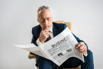 selective focus of mature businessman in glasses reading business newspaper isolated on grey
