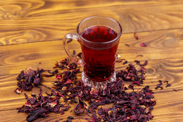 Glass cup of red hibiscus tea (carcade, roselle) on wooden table