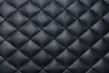 Black genuine leather texture background stitched with a thread across cross. Close up view from above.