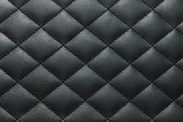 Dark grey genuine leather texture background stitched with a thread across cross. Close up view from above.