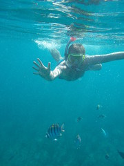 Young man in mask and snorkel dives with fishes. Underwater photo