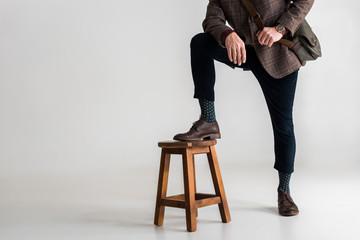 cropped view of stylish mature man putting leg on chair while standing on grey