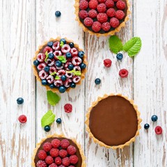 Raspberry and blueberry tartlets with chocolate ganache, fresh berries and mint leaves, selective focus. Fresh fruit tart on white background, freshly homemade fruit cake on a table