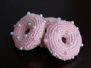 Knitted pink donuts on the black background is sewed from fabric for a children's game in a shop or cafe.
