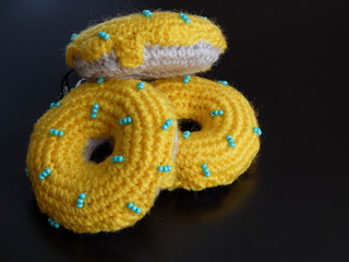 Knitted yellow donuts on the black background is sewed from fabric for a children's game in a shop or cafe.