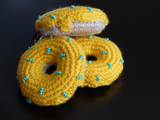 Knitted yellow donuts on the black background is sewed from fabric for a children's game in a shop or cafe.