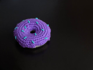 Knitted purple donut on the black background is sewed from fabric for a children's game in a shop or cafe.