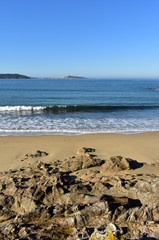 Beach with rocks, golden sand, waves and blue sky. Galicia, Spain.