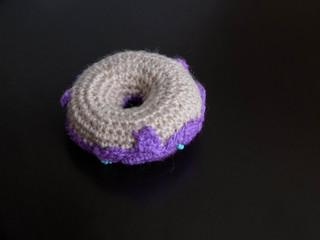 Knitted purple donut on the black background is sewed from fabric for a children's game in a shop or cafe.
