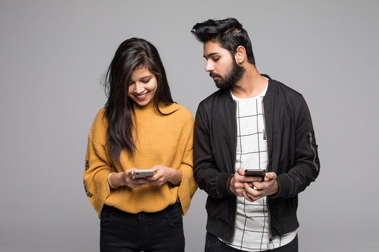 Curious indian boyfriend is spying his lovers smartphone standing isolated on gray background