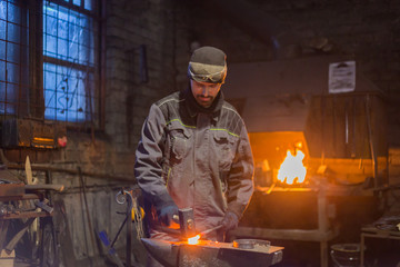 Professional blacksmith forging molten metal on anvil at smithy, workshop. Handmade, craftsmanship and blacksmithing concept