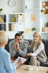 Blonde young woman explaining something to counselor while sitting on couch next to her husband