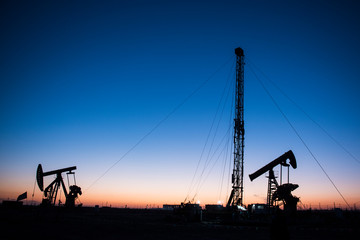 Oil pumps are running in the sunset at the oil field.