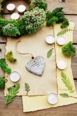 Wooden heart on paper background among moss and fern decorations.