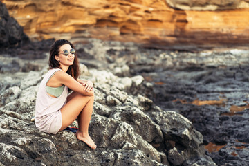 Pretty long hair brunette tourist girl relaxing on the stones near sea.