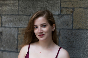 Medium horizontal portrait of exquisite blue-eyed young woman in velvet tank top with small smile standing against stone wall