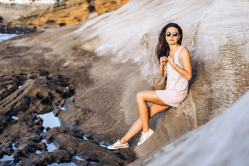 Pretty long hair brunette tourist girl relaxing on the stones near sea.