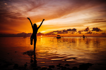 Free happy woman raising arms watching the sun in the background at purple sunset.
