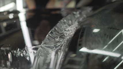 professional applying protective film to the red car. Master glues a protective film on the hood of...