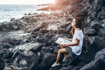 Pretty long hair tourist girl relaxing on the stones near sea.