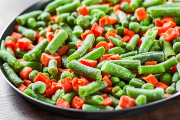 Mixed vegetables. green beans, peas and carrots in an iron pan on a wooden background