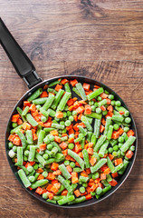 Mixed vegetables. green beans, peas and carrots in an iron pan on a wooden background