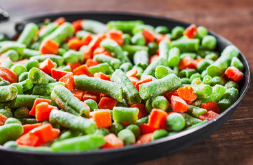 Mixed vegetables. green beans, peas and carrots in an iron pan on a wooden background