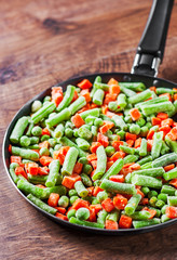 Mixed vegetables. green beans, peas and carrots in an iron pan on a wooden background