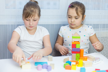 Obraz premium Children play with an educational toy on table in the children's room. Two kids playing with colorful blocks. Kindergarten educational games