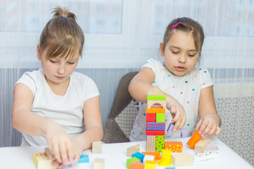Obraz na płótnie Canvas Children play with an educational toy on table in the children's room. Two kids playing with colorful blocks. Kindergarten educational games