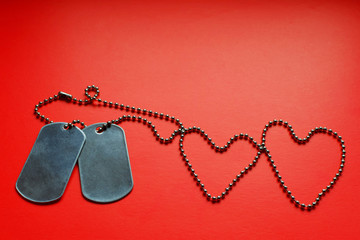 Two blank silver color soldier military tags on ball chain in shape of heart on red background with copy space for text.