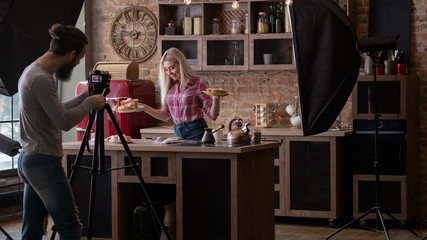 Homemade bakery. Cooking blog. Backstage photography. Man with camera shooting young woman with pastries.