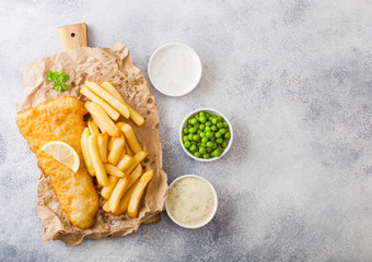 Traditional British Fish and Chips with tartar sauce on chopping board and green peas on white...