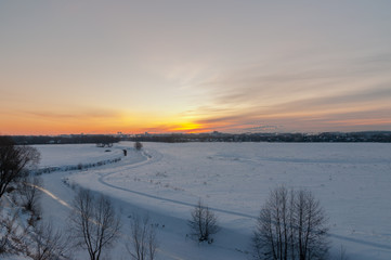 Winter sunrise at the river cliffs with the river encased in ice, snowed plains and a city in the distance