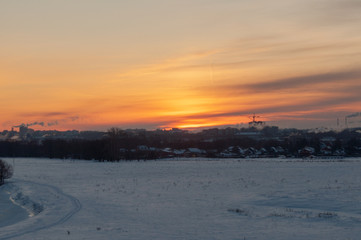 Winter sunrise at the river cliffs with the river encased in ice, snowed plains and a city in the distance