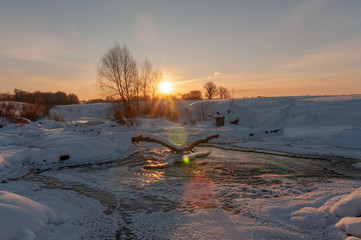 Rising sun over the frozen river with ice, snow and the running water