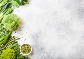 Assorted green toned raw organic vegetables on white stone background. Avocado, cabbage, broccoli,...