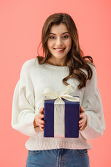 smiling and attractive woman in white sweater holding gift box isolated on pink