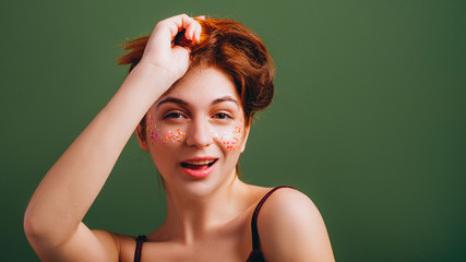 Cute young woman portrait. Redhead female messing hair. Fun and flirty mood. Copy space on green...