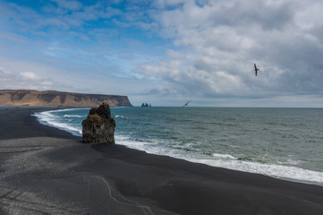 Kamienna czarna plaża z samotną skałą nad oceanem