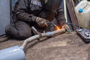 repairing of corrugation muffler of exhaust system in car workshop - serviceman welds the old...