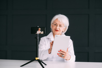 Successful senior female. Fashion trends blogger. Smart aged lady with tablet making business video tutorial.