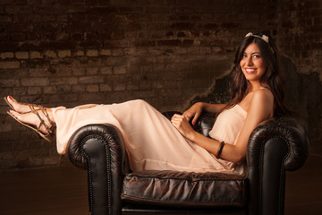 Fototapeta na wymiar pretty brunette girl sitting on leather sofa with brick wall background