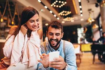 Young happy couple using smartphone in cafe