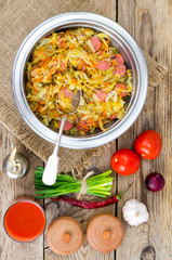 Fried sauerkraut with sausages in metal bowl.