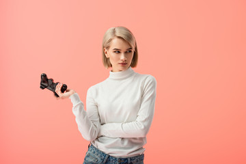 upset blonde woman holding joystick while standing isolated on pink © LIGHTFIELD STUDIOS