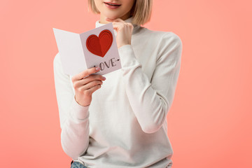 cropped view of woman holding greeting card while standing isolated on pink