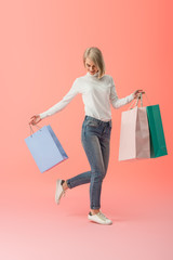 happy blonde young woman holding shopping bags on pink background