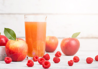Glass of fresh organic apple and raspberry juice with fresh fruits in box on wooden background with sun light
