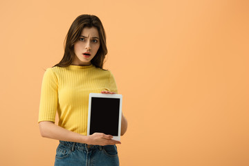 Dissatisfied brunette girl holding digital tablet with blank screen isolated on orange
